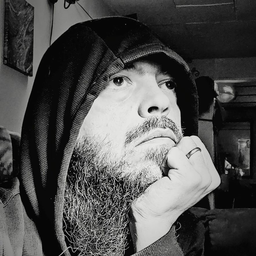 Warren is showin in black and white, pensively looking to the right, chin propped on his left hand, wedding ring prominently displayed. You see his long beard