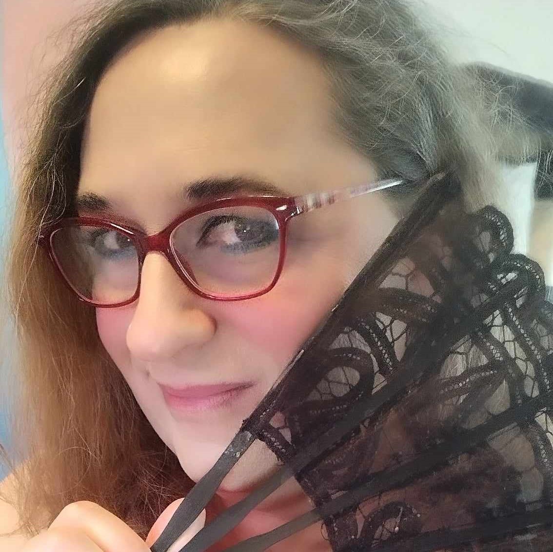 Vanna is shown wearing red glasses with clear arms, smiling coyly behind a black lace fan.