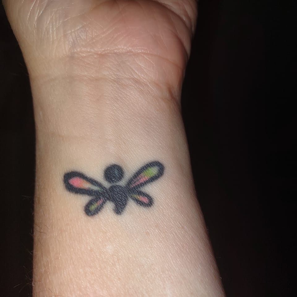 Photo of Zen's semicolon tattoo that has dragon wings of rainbow colors with a semicolon body on her wrist