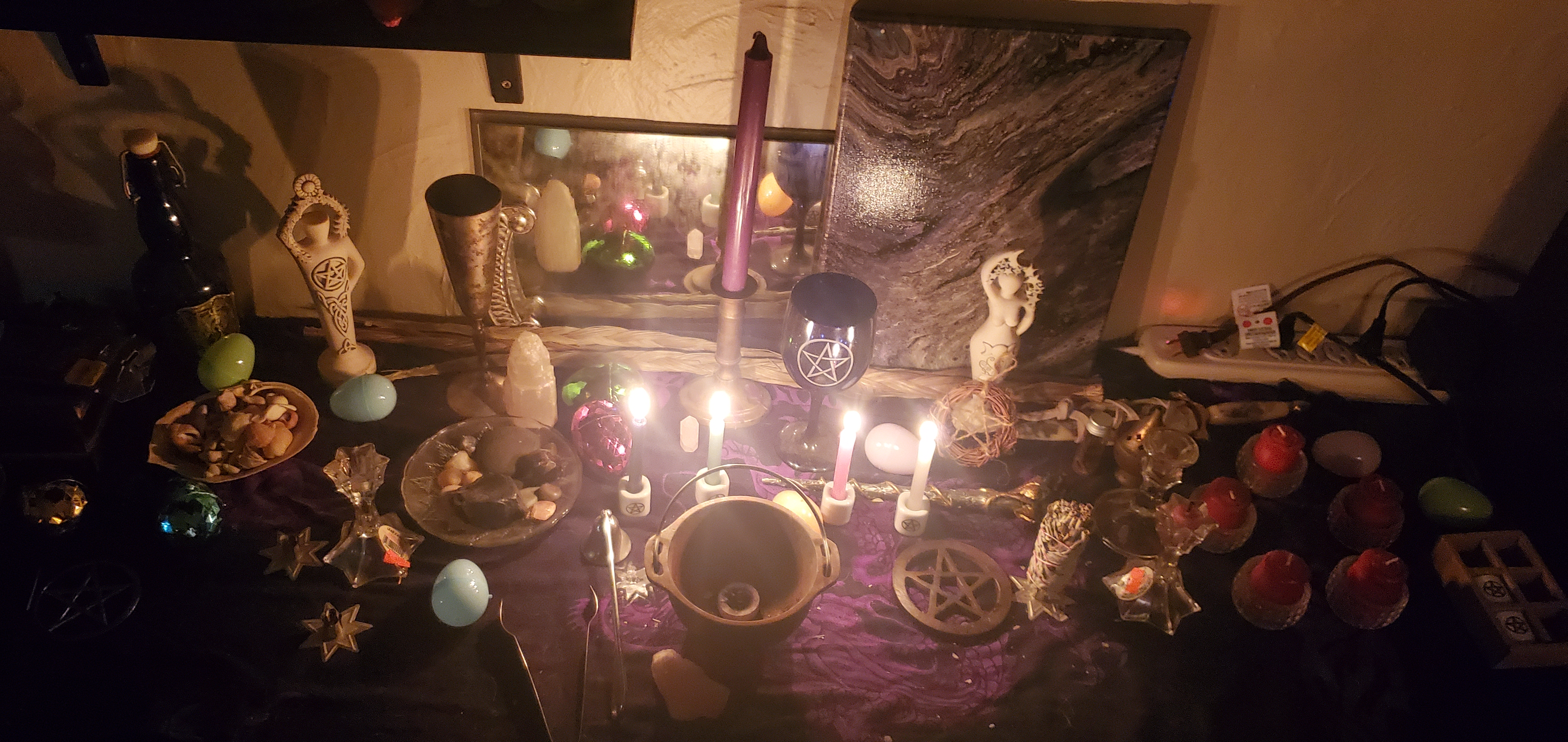 Di's altar during an Ostara working. Plastic eggs, a cast iron cauldron, lit chime candles, a wooden pentacle, god and goddess statues,& a cobalt glass chalice