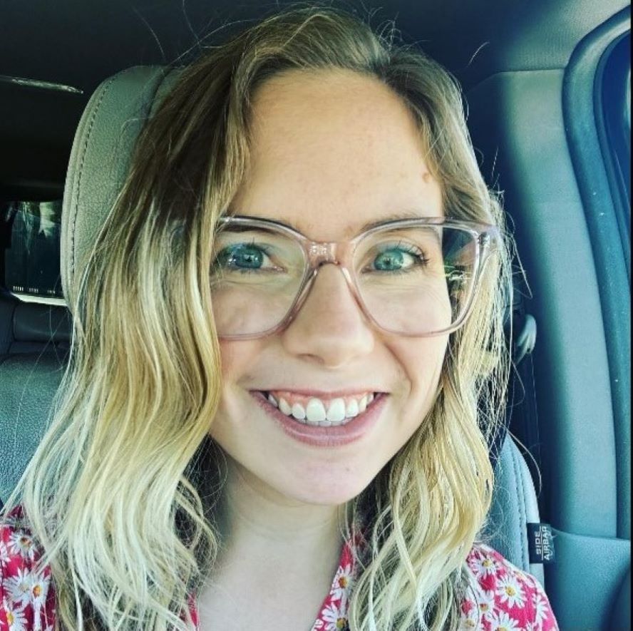 Alysa is a cute blonde woman with big glasses and an even bigger smile. Blonde wavy hair frames her face as she smiles at the camera. She is wearing a red top